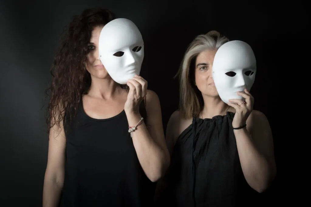 Dos mujeres sostienen máscaras blancas delante de sus rostros